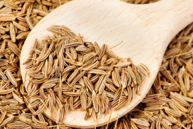 cumin seeds and wooden spoon as background cumino proprieta benefiche ricette