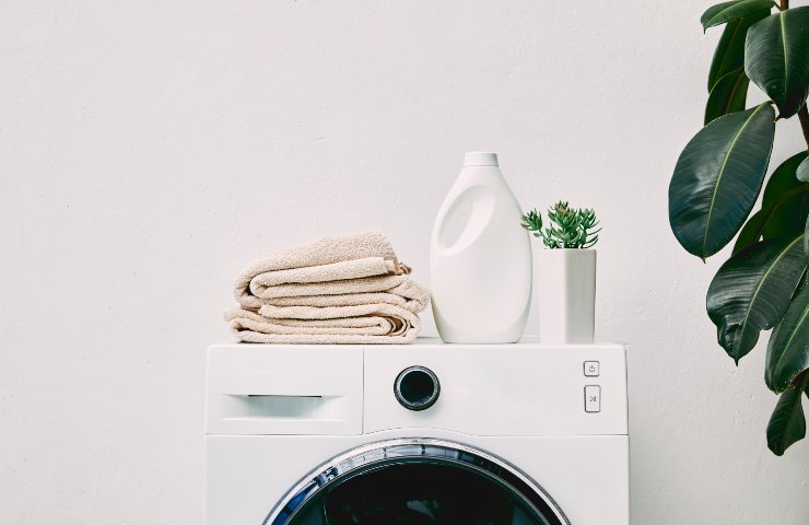 Una lavatrice con asciugamani ed un detersivo sopra