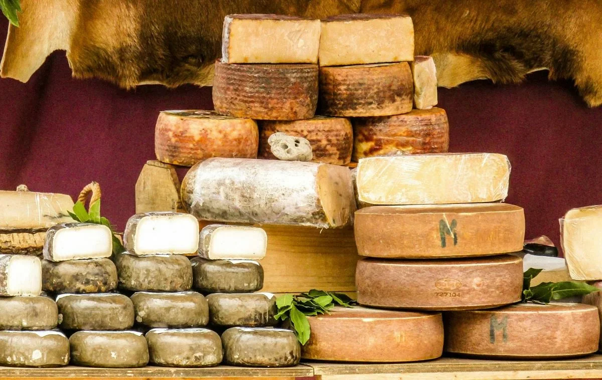 Selezione di forme di formaggio stagionato artigianale impilate su un banco del mercato.